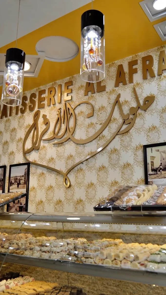 Notre enseigne en lettres dorées « Pâtisserie Al Afrah » et la calligraphie arabe حلويات الأفراح, au-dessus des vitrines et sous deux suspensions de verre.
