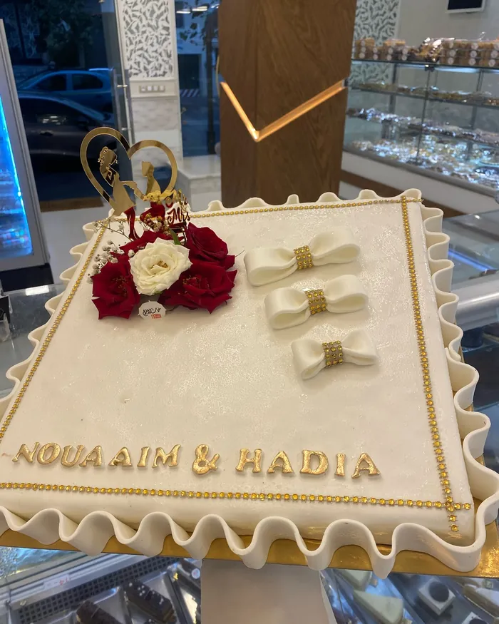 Gâteau de mariage à trois étages, glaçage blanc travaillé en dentelle, roses rouges fraîches, gypsophile et monogramme doré, sur commande.
